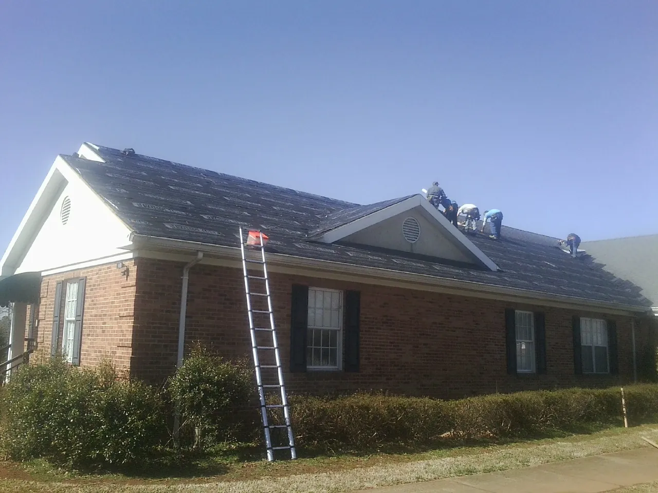Crew tearing shingles off a brick ranch roof with a ladder set — Metal Roof Repair work by our crew in Cadiz