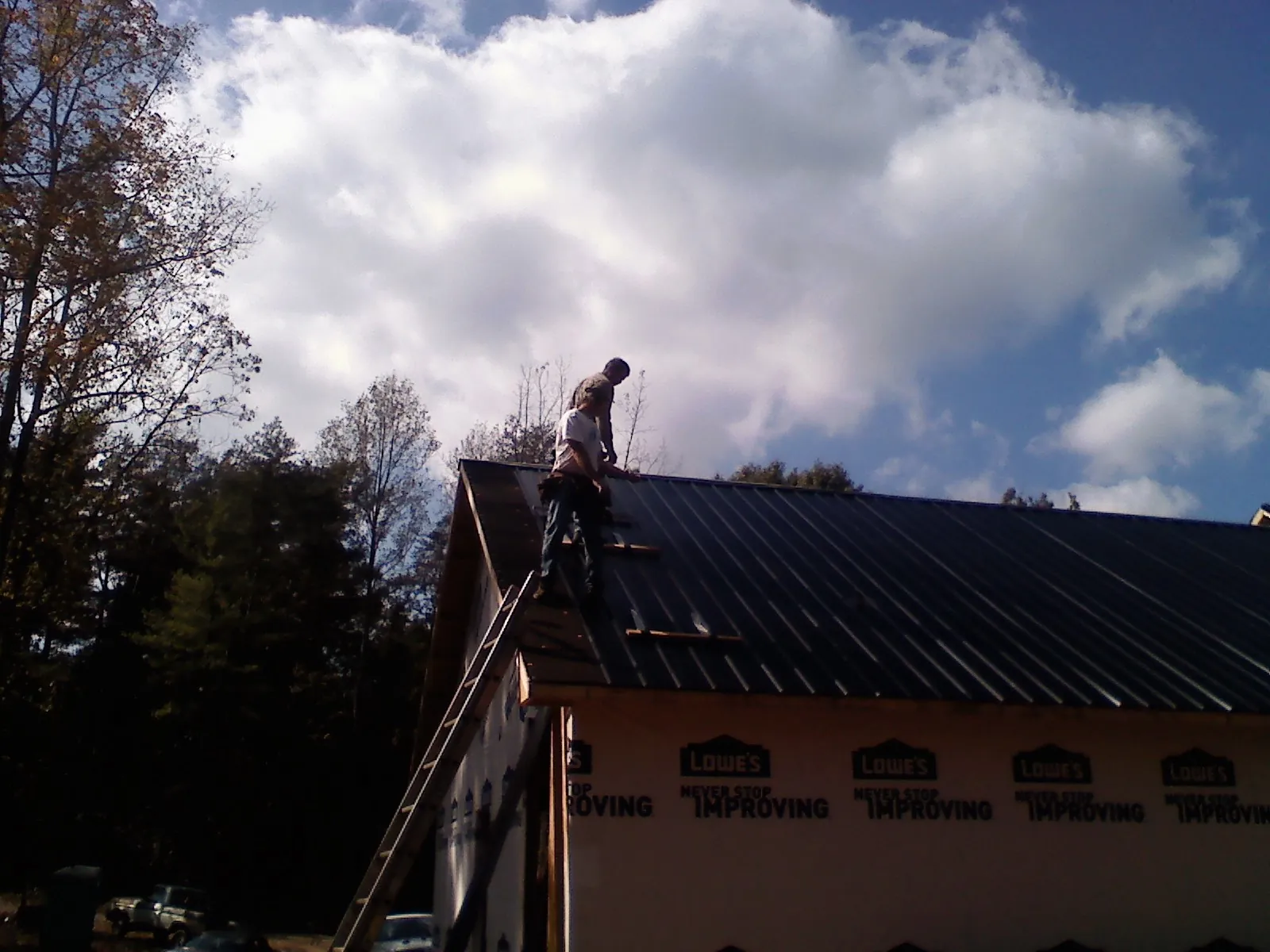 Roofer fastening dark metal panels high against a cloudy sky, from a Roof Inspection job in Cadiz