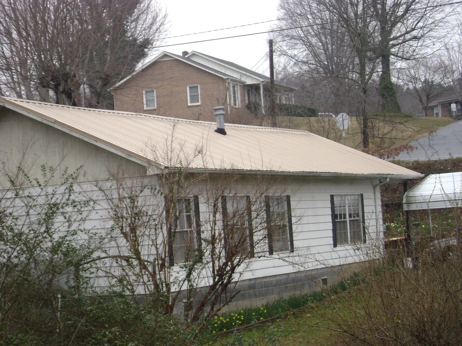 Tan metal roof on a white sided house set into a hillside — Commercial Roofing by Roofing Brothers in Cadiz